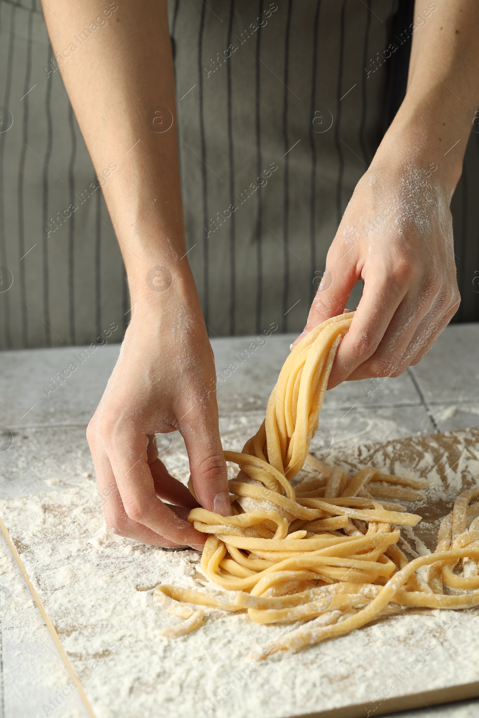 Photo of Woman with homemade pasta at light tiled table, closeup