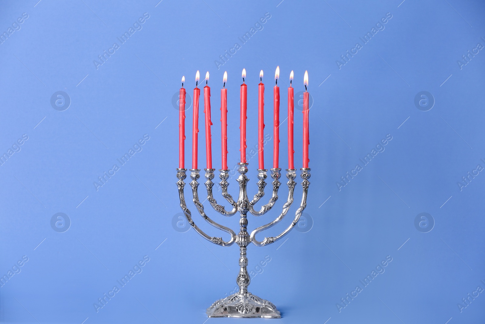 Photo of Silver menorah with burning candles on light blue background. Hanukkah celebration