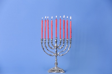 Photo of Silver menorah with burning candles on light blue background. Hanukkah celebration