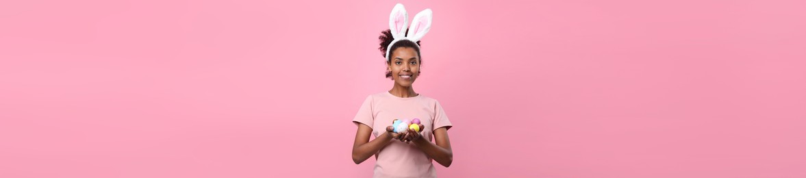 African American woman with bunny ears holding Easter eggs on pink background. Banner design