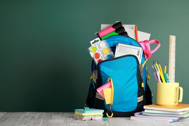 Backpack with different school stationery on wooden table near chalkboard, space for text