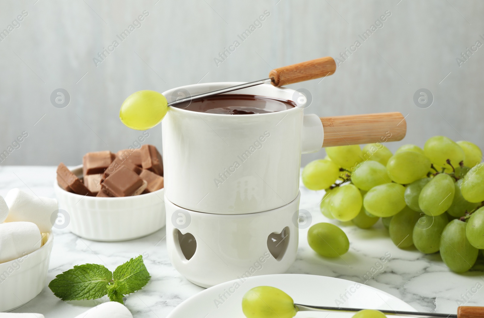 Photo of Fondue pot with dark chocolate and grapes on marble table