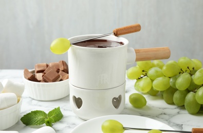 Photo of Fondue pot with dark chocolate and grapes on marble table