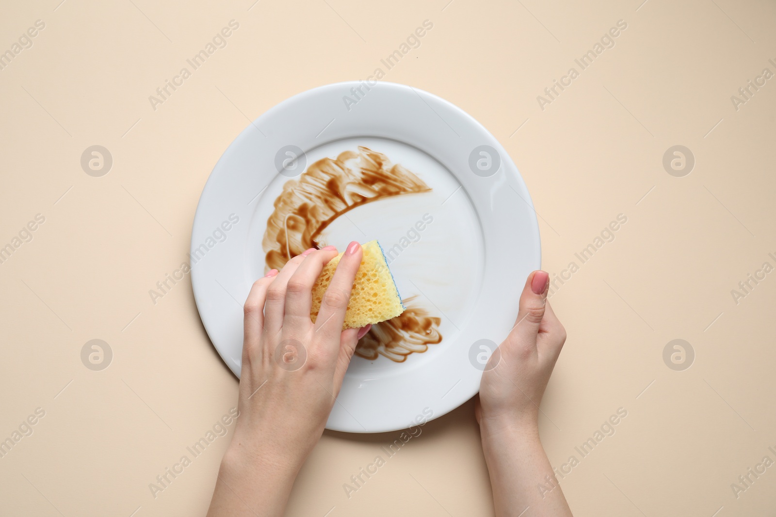 Photo of Woman washing dirty plate with sponge on beige background, top view