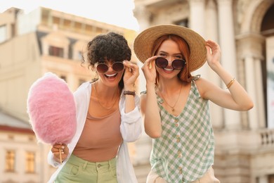 Photo of Happy friends with pink cotton candy outdoors on sunny day