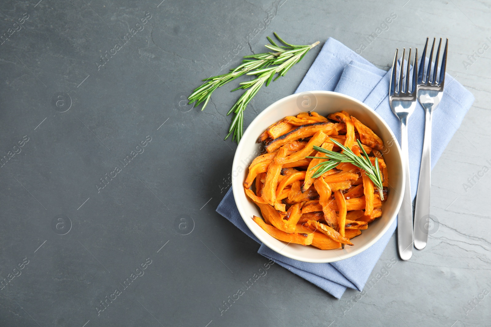 Photo of Bowl with baked sweet potato slices served on grey table, top view. Space for text