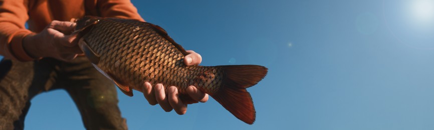 Image of Fisherman holding caught fish against blue sky, closeup view with space for text. Banner design