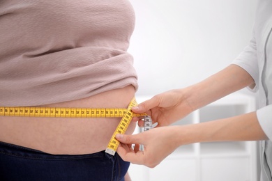 Photo of Doctor measuring waist of overweight woman in clinic, closeup