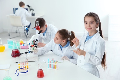 Photo of Smart pupils making experiment at table in chemistry class