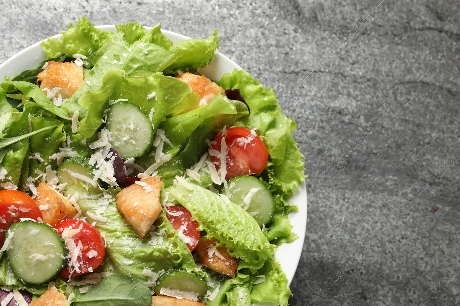 Photo of Delicious salad with chicken, cheese and vegetables on grey table, top view. Space for text
