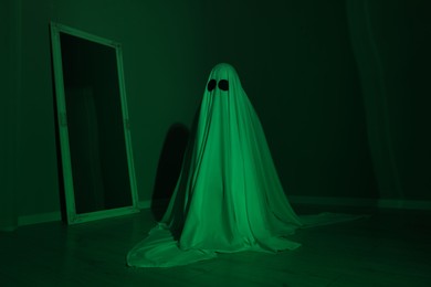 Photo of Creepy ghost. Woman covered with sheet in green light