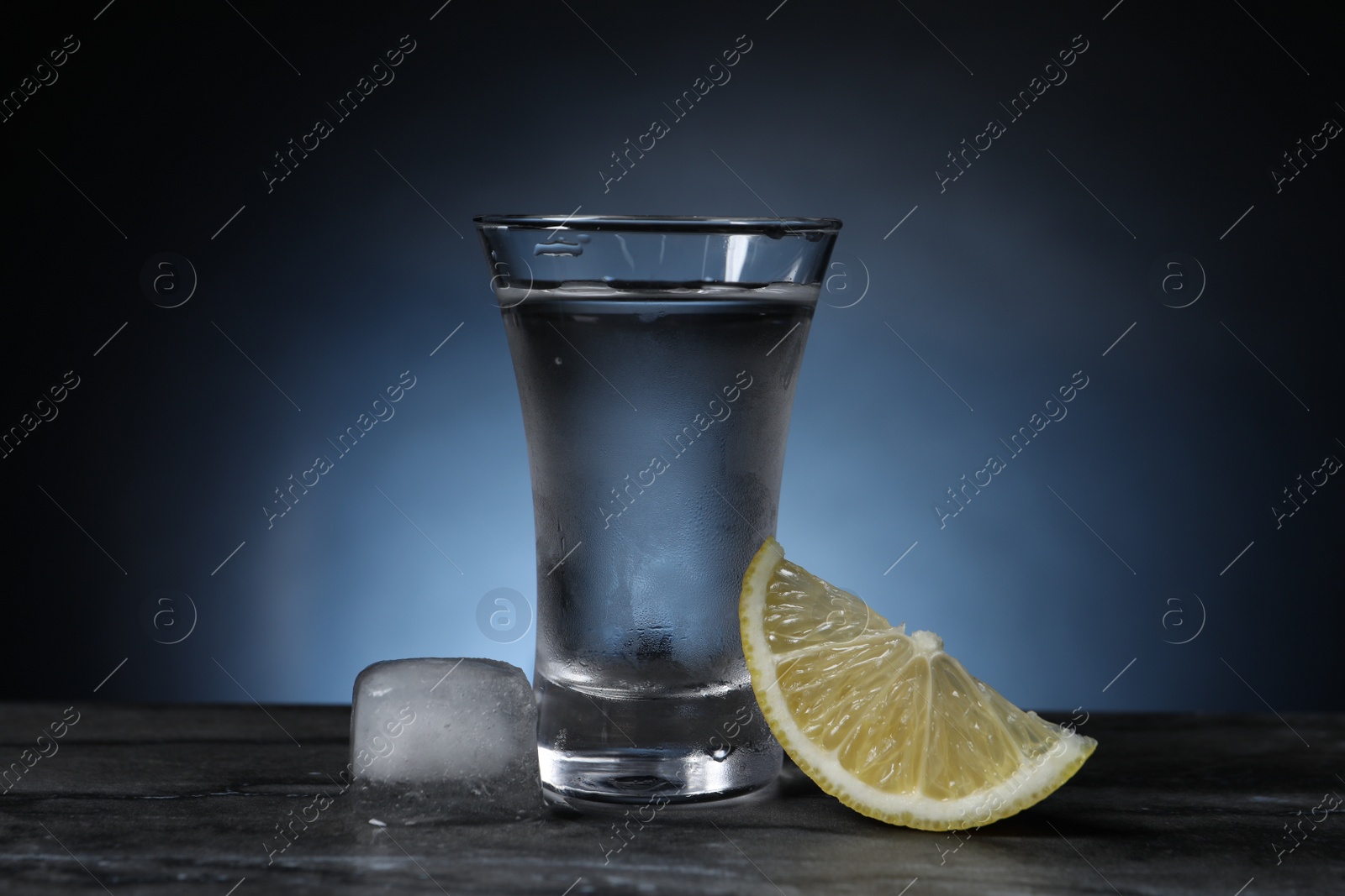 Photo of Shot of vodka with lemon slice and ice on grey table