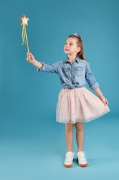 Photo of Cute girl in diadem with magic wand on light blue background. Little princess