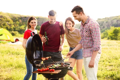Photo of Young people having barbecue in wilderness. Camping season