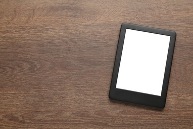 Photo of Modern e-book reader with blank screen on wooden table, top view. Space for text