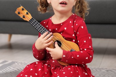 Little girl playing toy guitar at home, closeup