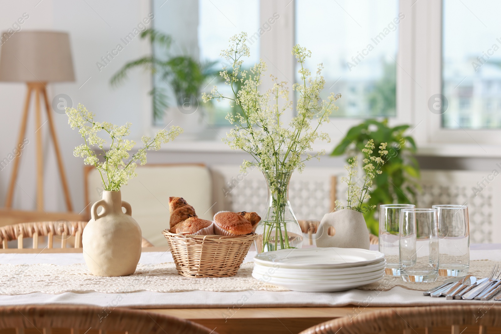 Photo of Clean dishes, flowers and fresh pastries on table in stylish dining room