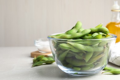 Photo of Bowl with green edamame beans in pods on light grey table. Space for text