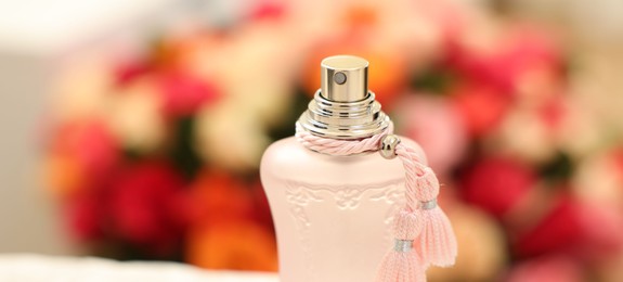 Photo of Bottle of perfume against beautiful roses, closeup and space for text. Banner design