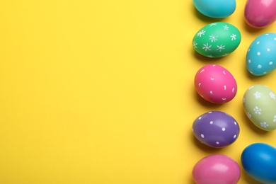 Photo of Bright painted eggs on yellow background, flat lay with space for text. Happy Easter