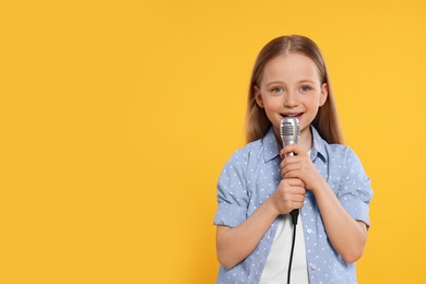 Photo of Cute little girl with microphone singing on yellow background, space for text