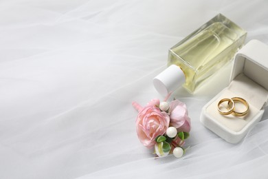 Photo of Wedding stuff. Stylish boutonniere, wedding rings and perfume bottle on white veil, closeup. Space for text