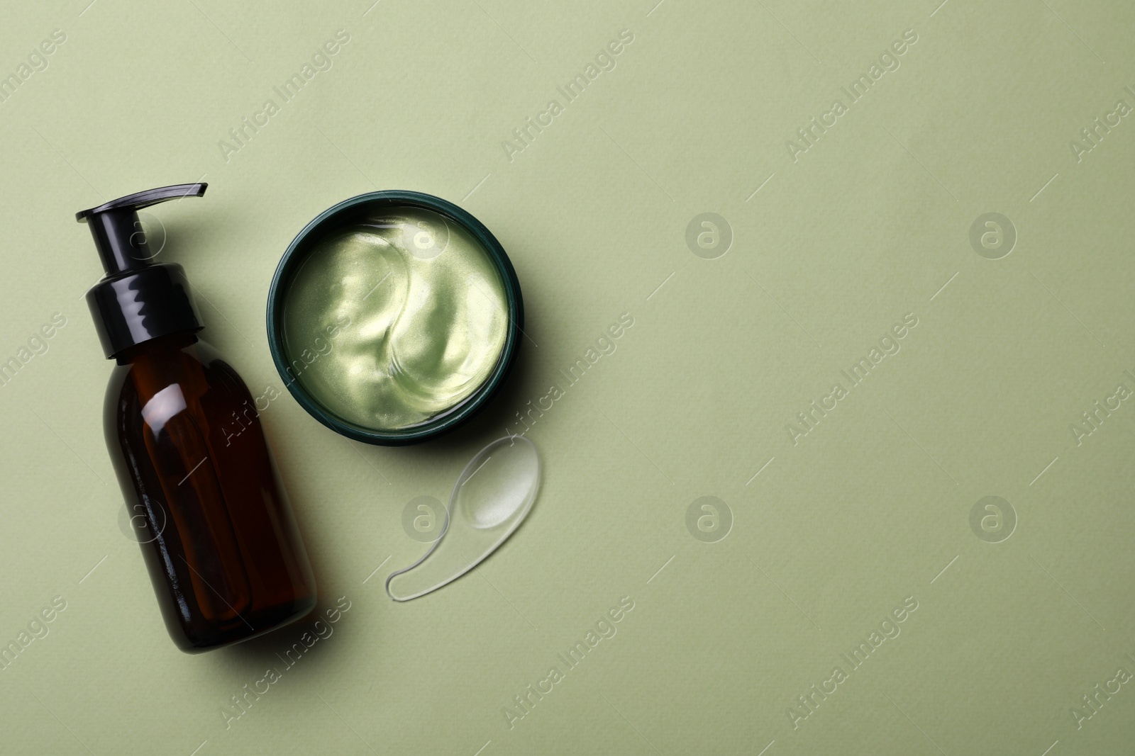 Photo of Under eye patches in jar with spatula and bottle of cosmetic product on olive background. Space for text