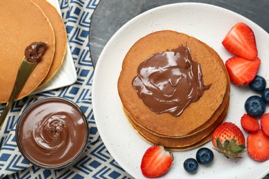 Photo of Tasty pancakes with chocolate paste and berries served on table, flat lay