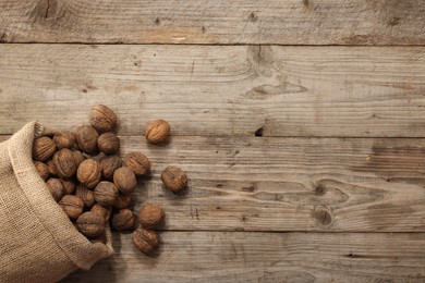 Burlap sack with walnuts on wooden table, top view. Space for text