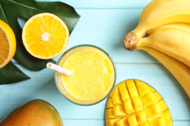 Glass of fresh mango drink and tropical fruits on color wooden background, top view