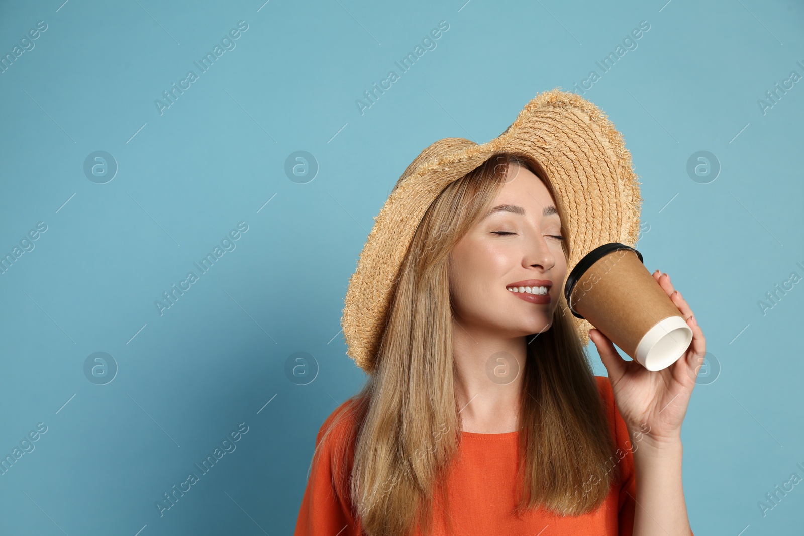 Photo of Beautiful young woman with straw hat drinking coffee from paper cup on light blue background, space for text. Stylish headdress