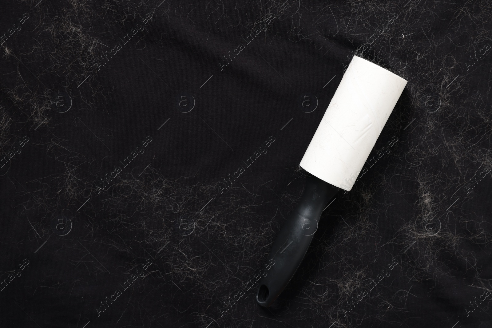 Photo of Removing pet hair with lint roller from black fabric, top view. Space for text