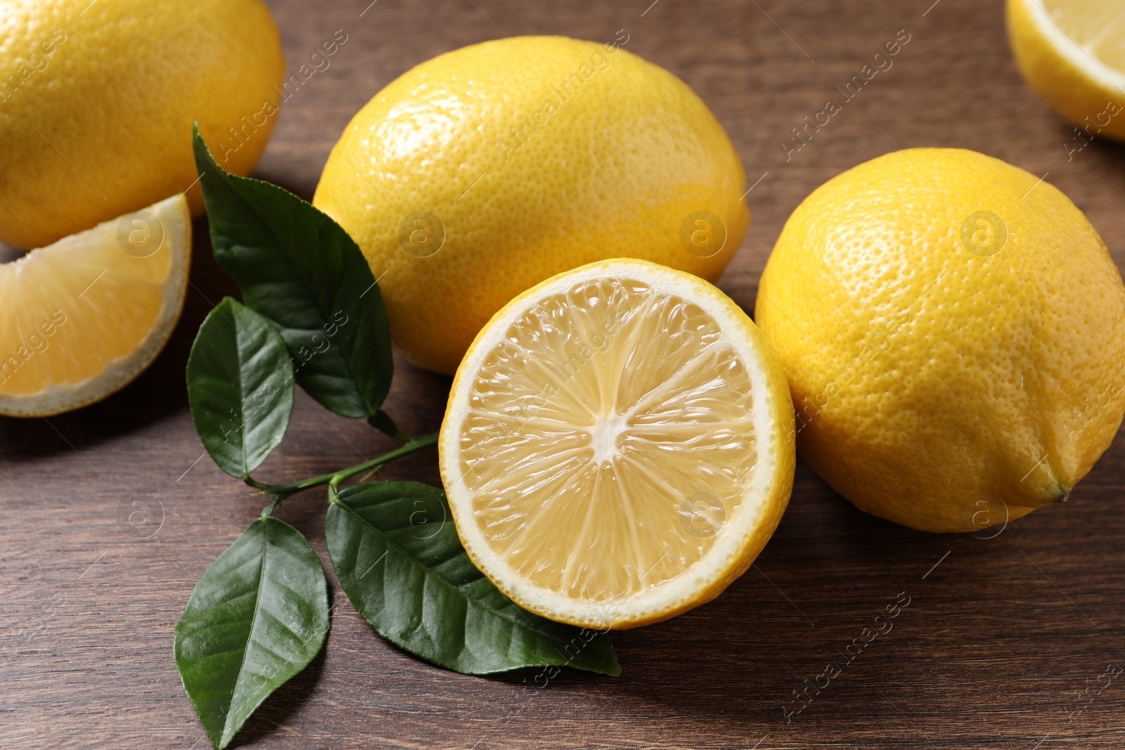 Photo of Fresh lemons and green leaves on wooden table, closeup