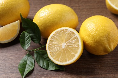 Fresh lemons and green leaves on wooden table, closeup