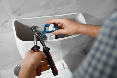 Photo of Professional plumber repairing toilet in bathroom, closeup