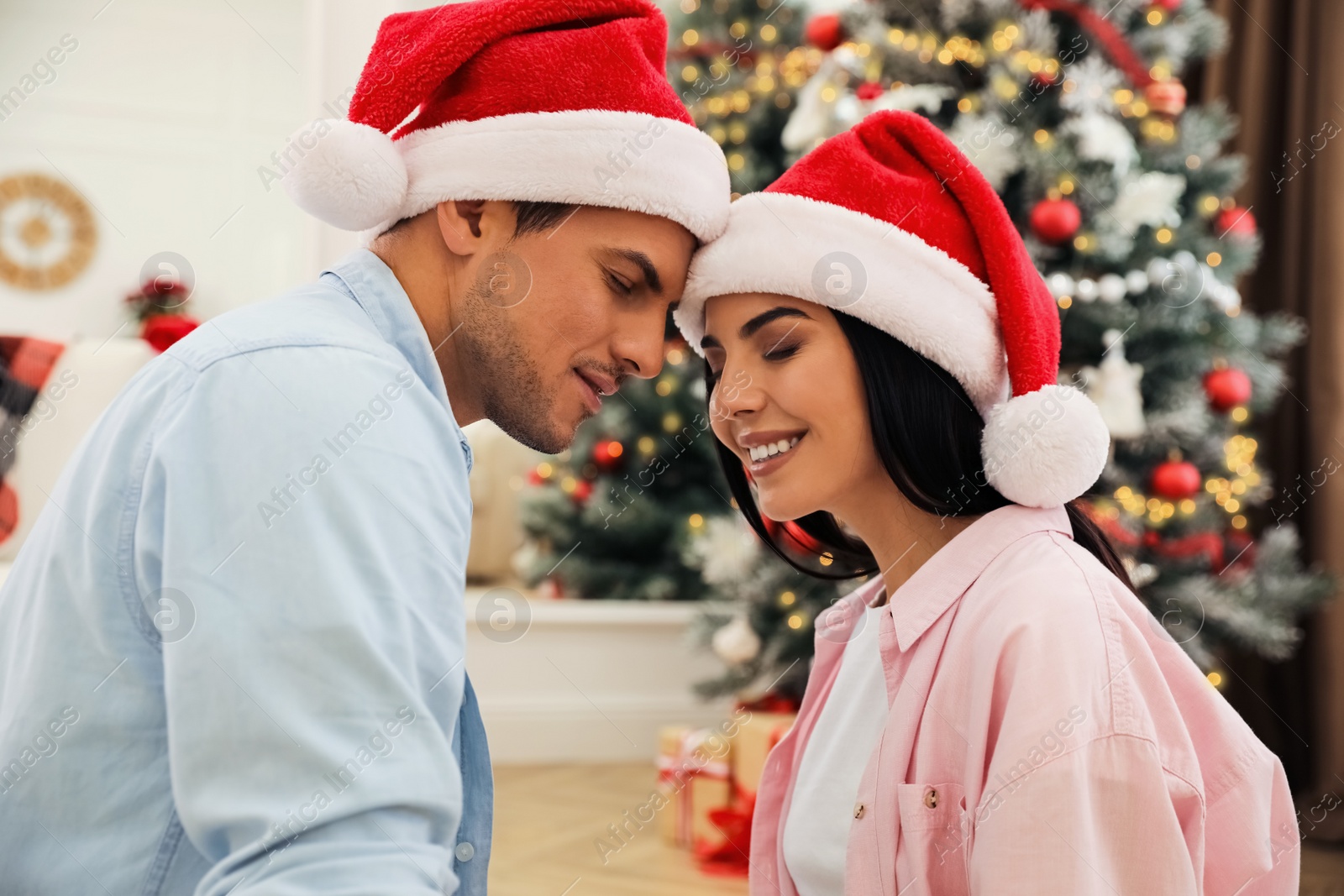 Photo of Happy couple in Santa hats near Christmas tree at home