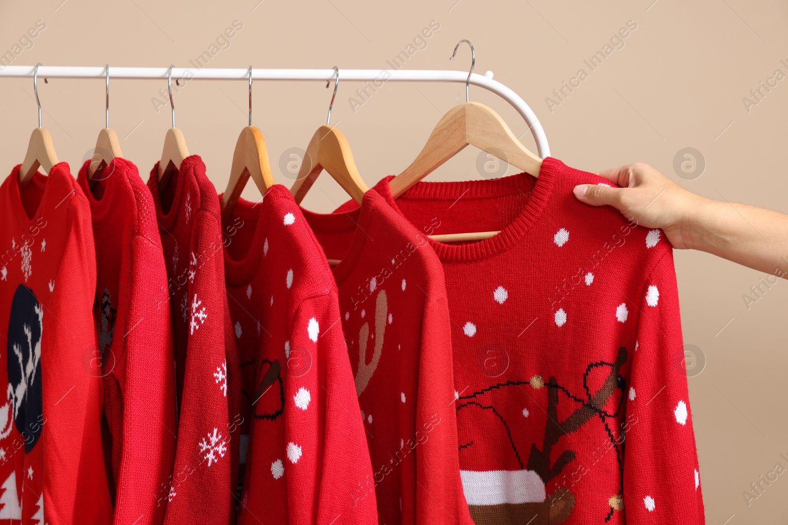 Photo of Woman choosing Christmas sweater from rack near beige wall, closeup