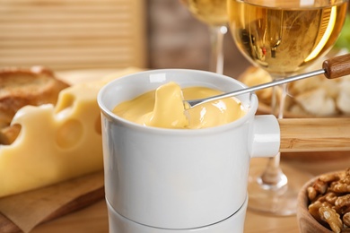 Pot of tasty cheese fondue and fork with bread on table