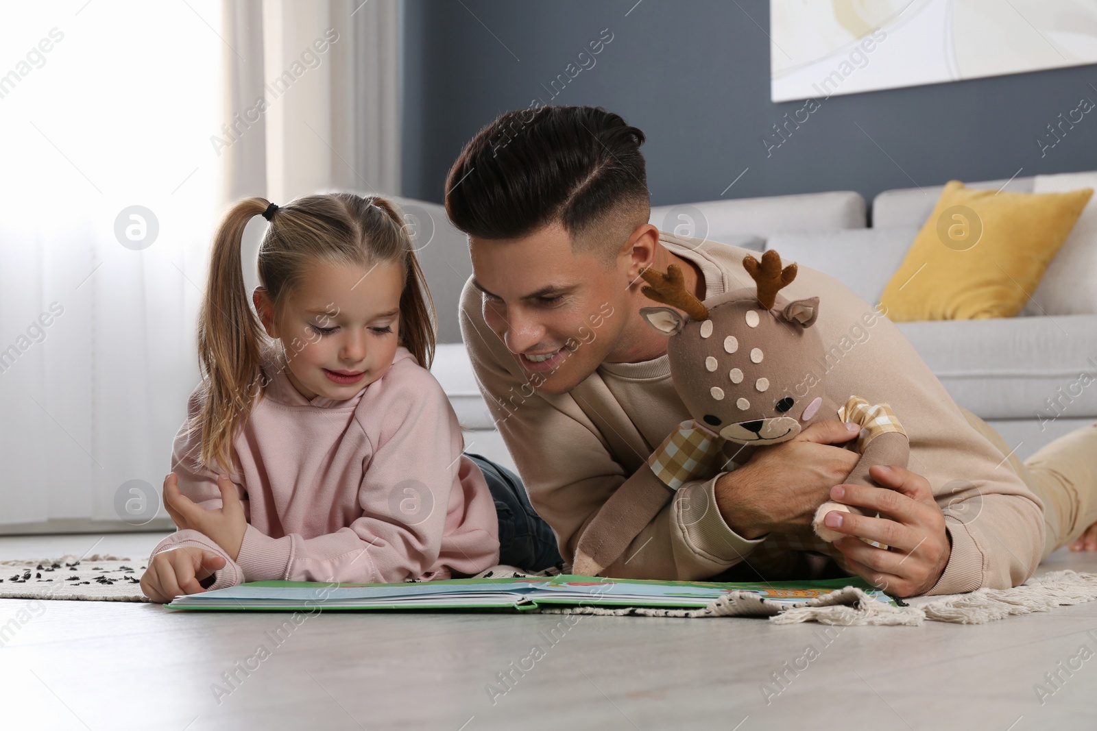 Photo of Father and his daughter reading book at home. Floor heating concept