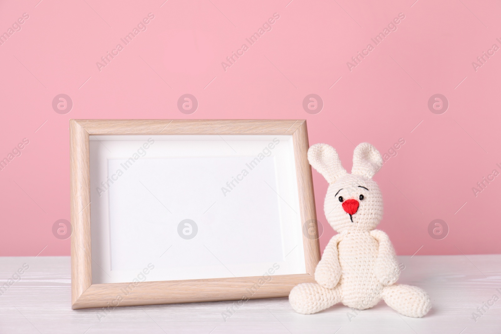 Photo of Photo frame with space for text and adorable toy bunny on table against color background. Child room elements