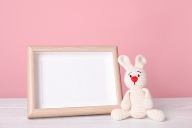 Photo frame with space for text and adorable toy bunny on table against color background. Child room elements
