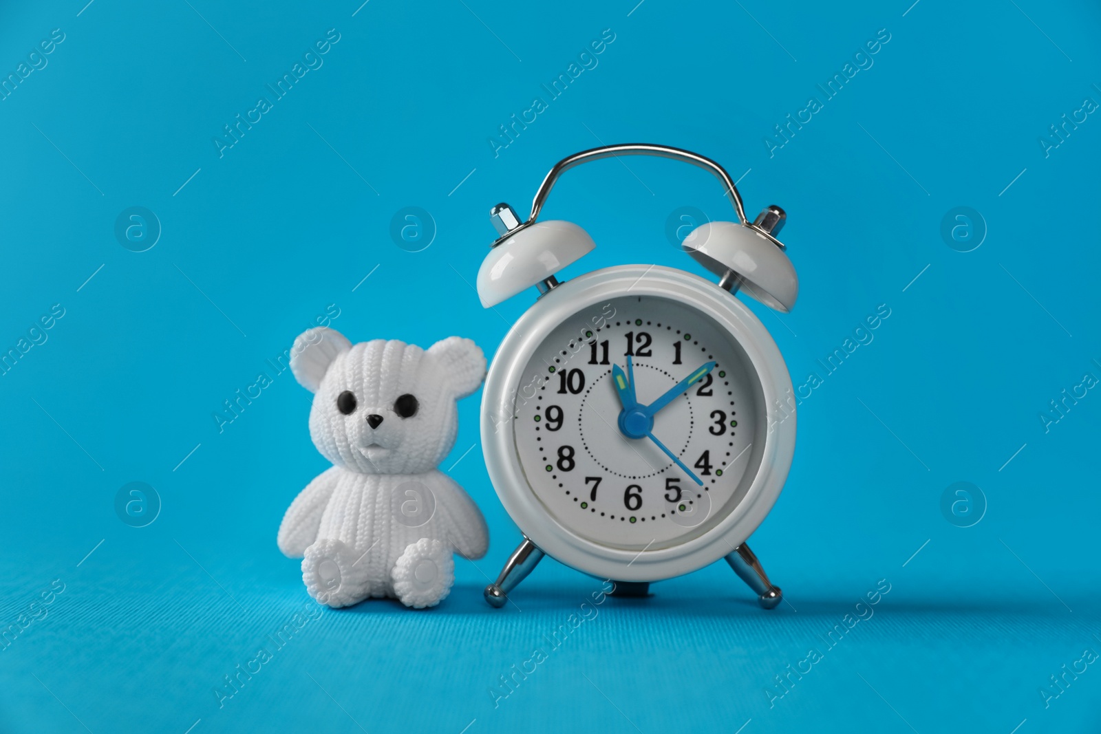 Photo of Alarm clock and toy bear on light blue background. Time to give birth