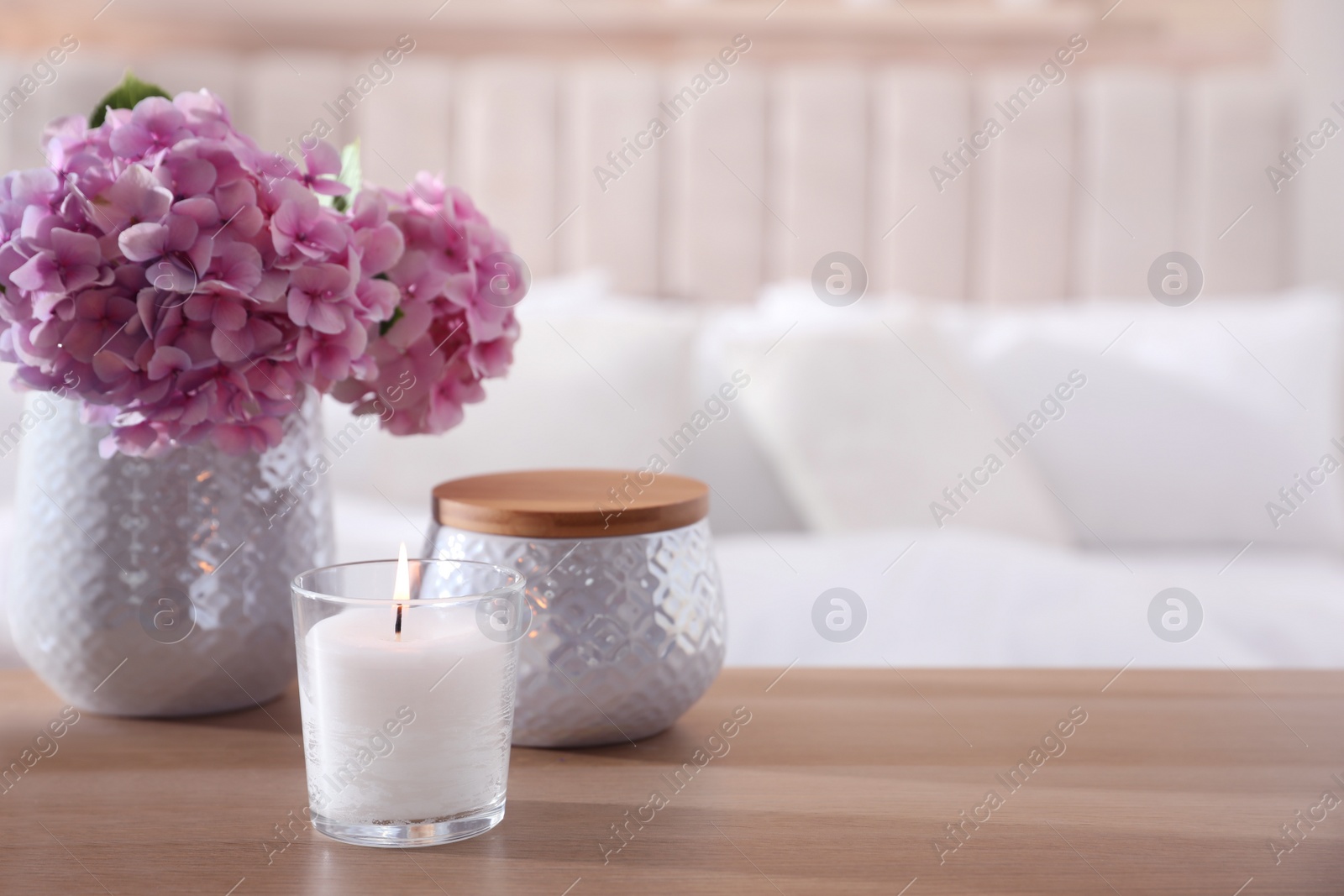 Photo of Burning candle and beautiful flowers on wooden table indoors. Space for text