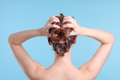 Photo of Young woman washing her hair with shampoo on light blue background, back view