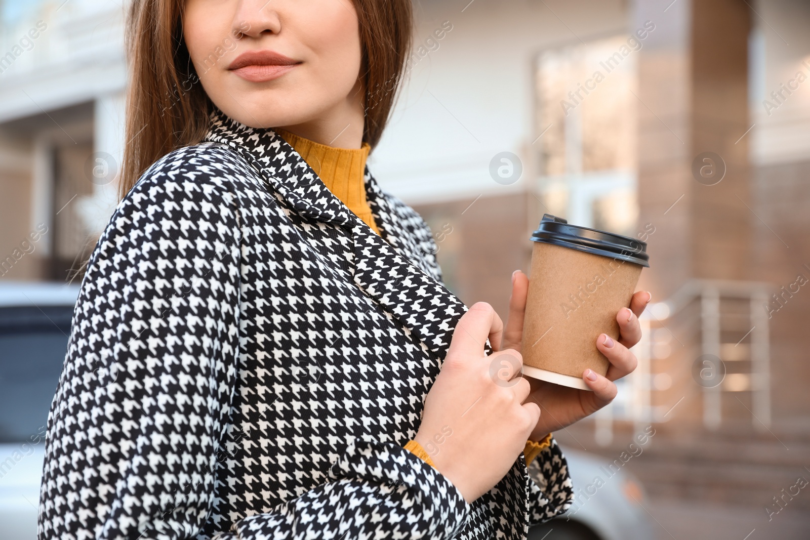 Photo of Young woman with cup of coffee on city street in morning, closeup