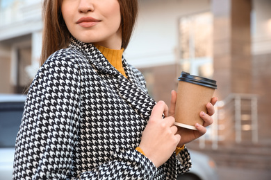 Young woman with cup of coffee on city street in morning, closeup