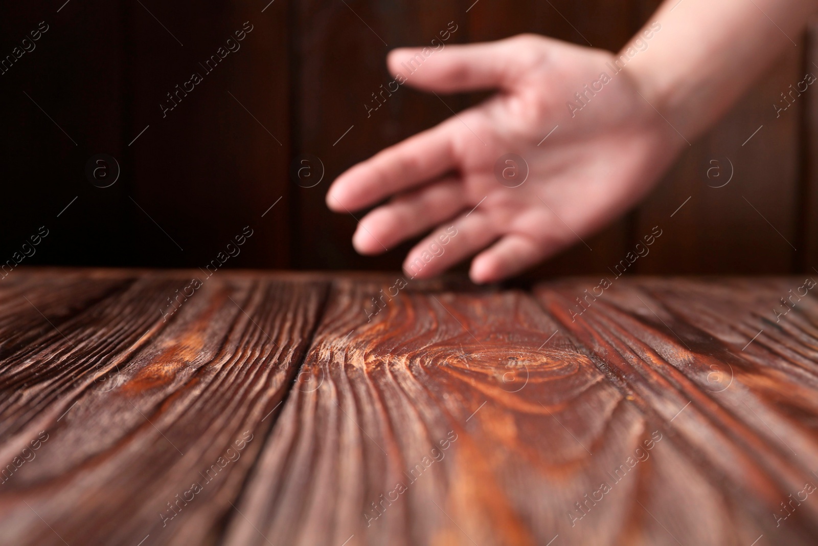 Photo of Woman holding hand above wooden table, selective focus. Space for text