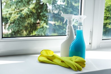 Photo of Spray bottles of detergents and gloves on window sill indoors, space for text. Cleaning supplies