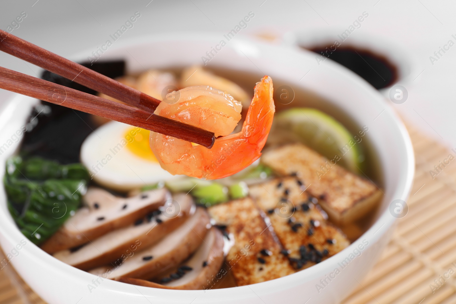 Photo of Eating delicious ramen with chopsticks at table, closeup. Noodle soup