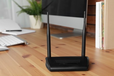 Photo of Modern wi-fi router near computer on wooden table